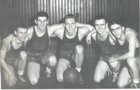 Five Scottsburg players in dark jerseys kneeling arm in arm around a basketball, in an old gym