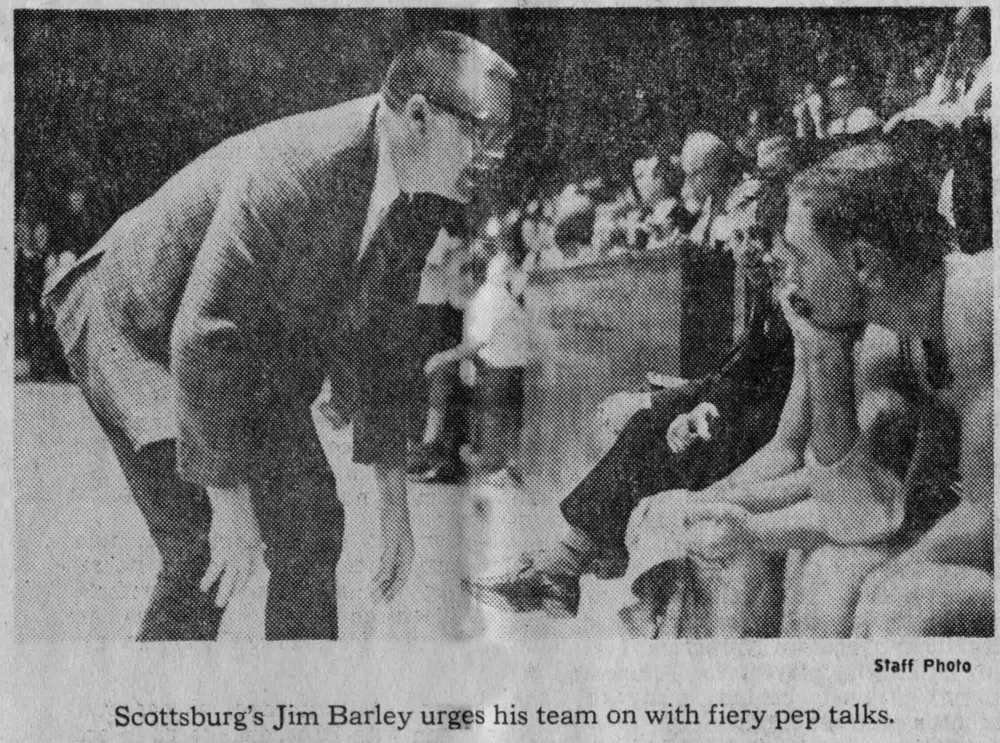 Newspaper photo: Jim Barley, in a suit, leans in to talk to his players on the bench