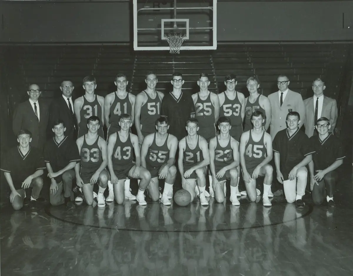 The 1968–69 Scottsburg Warriors in dark uniforms with their coaches and managers, under a basket