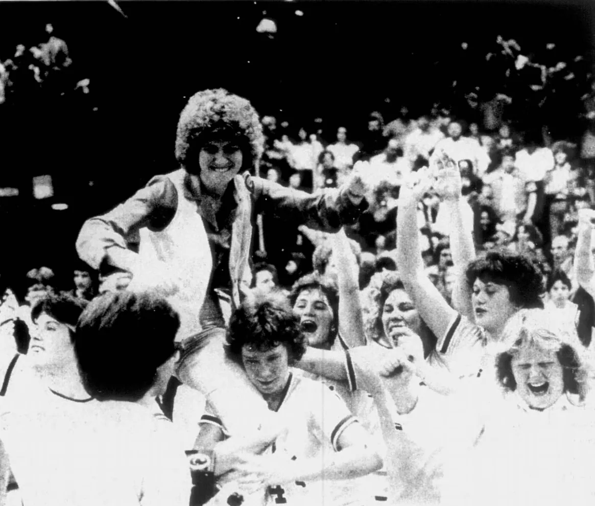 Newspaper photo: Donna Cheatham, in a fur hat, laughing on her players' shoulders, the Warriorettes cheering around her and the packed stands behind