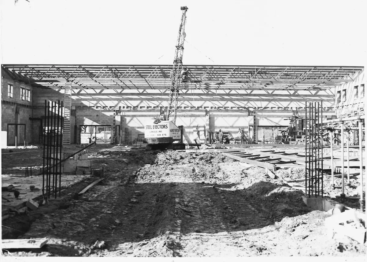 The gym under construction: the roof steel up on its joists, a crane in the middle, bare block walls and mud where the court will be
