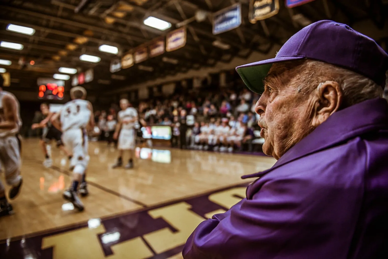 Gene Rogers, in a purple cap and jacket, watches a Warriors game from the edge of the floor