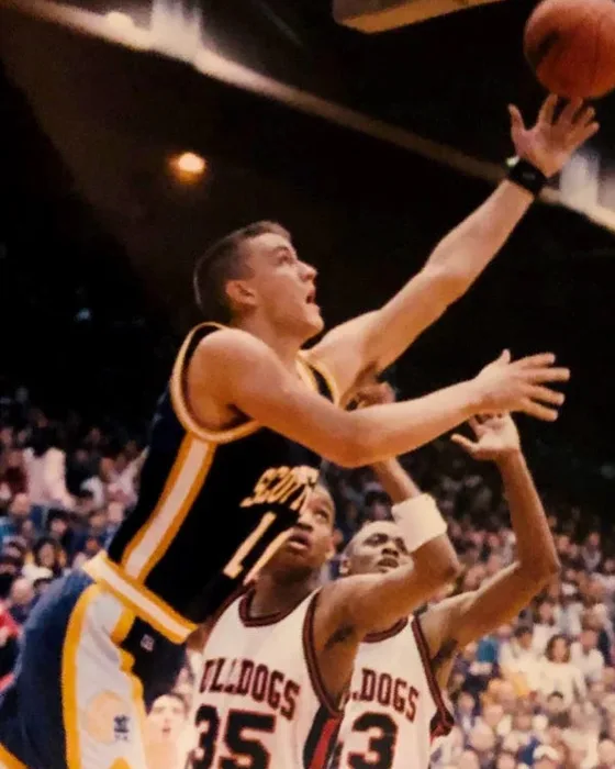 B.J. Watts reaching for a layup in a dark Scottsburg uniform, two defenders below him